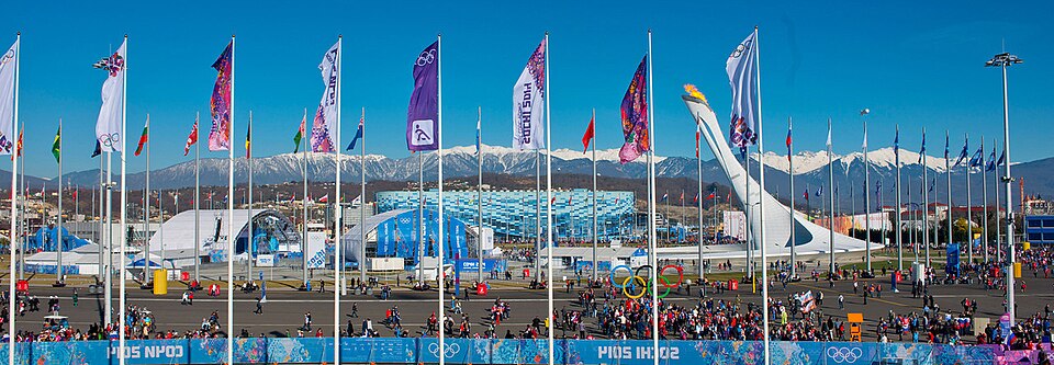 Crowds and Olympic flags at the Sochi Olympic Park during the 2014 Winter Olympics with the Caucasus Mountains in the background